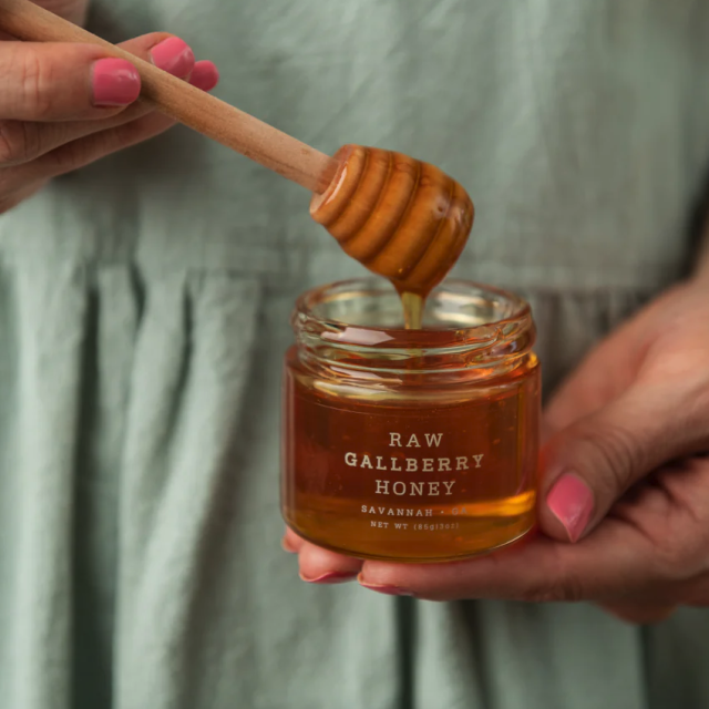 Hands holding a honey jar with honey dipper