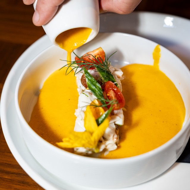 yellow gazpacho soup being poured into a bowl