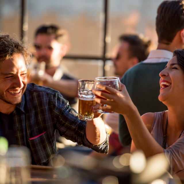 A man and a woman cheering with drinks in a lively restaurant.