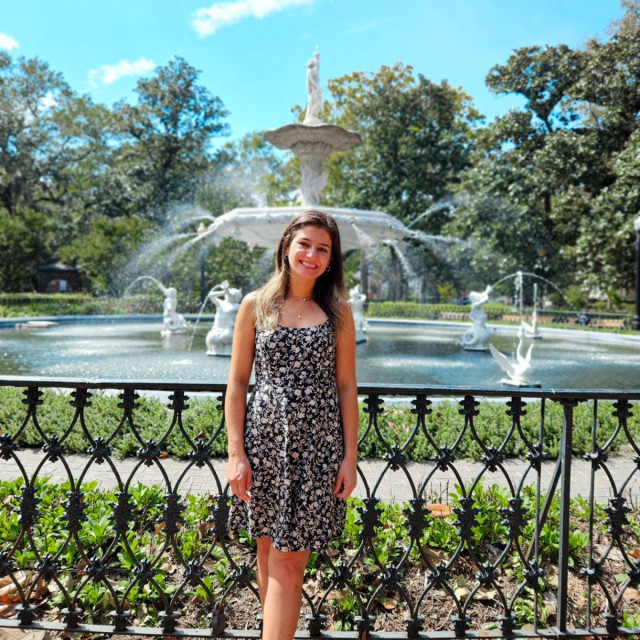 A young woman posing in front of a white fountain in a park.