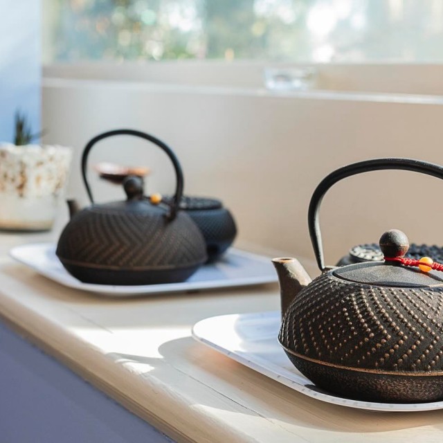 A row of tea kettles sitting along a window sill.