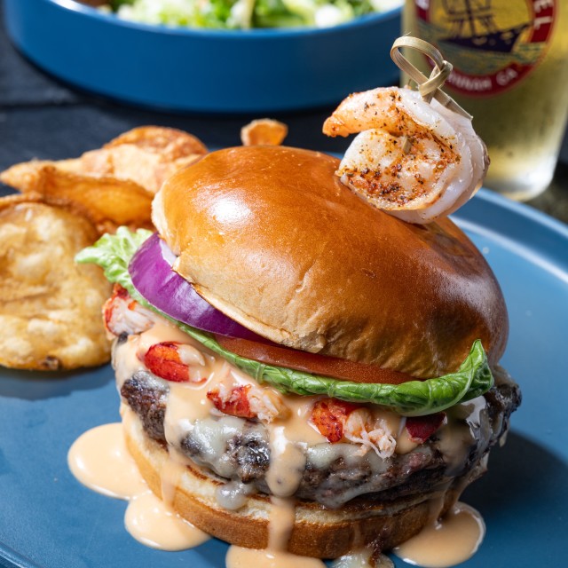 A burger served with chips, salad and a beer.