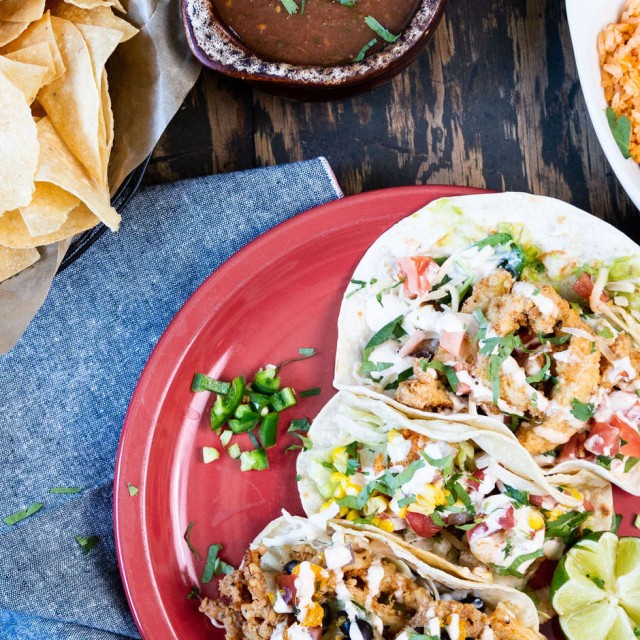 A plate of three soft tacos, chips and salsa, beans and rice on a table.