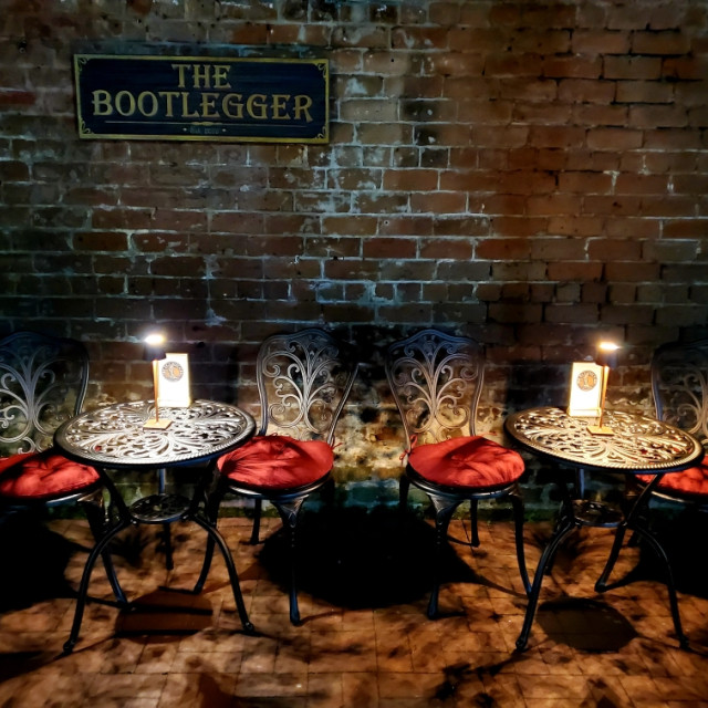 Two sets of bistro tables and chairs with red cushions and small lamps.