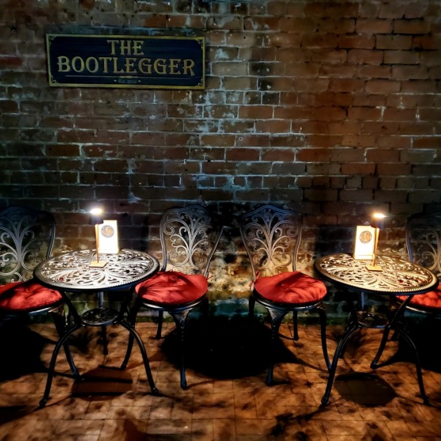 Two sets of bistro tables and chairs with red cushions and small lamps.