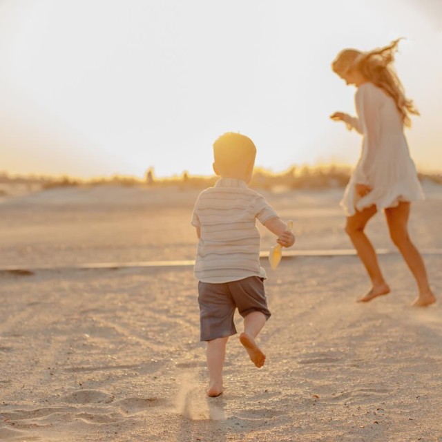A mother and child playing on the beach at sunset.