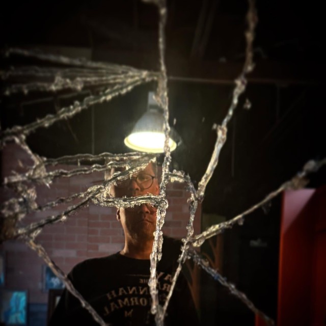 A creepy image of a man standing in front of a broken mirror.