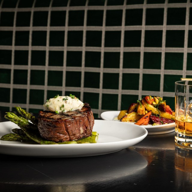 Filet mignon on a bed of asparagus topped with butter served on a white plate.