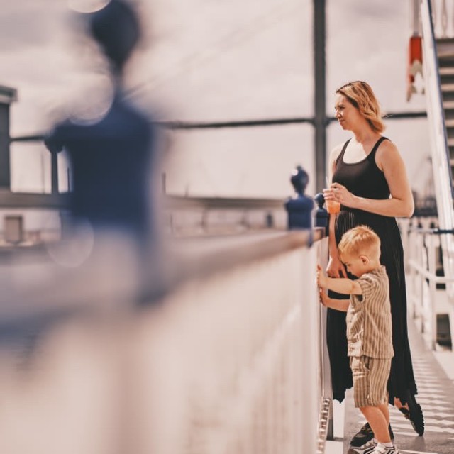 A mother and son enjoying the outdoor deck while on a riverboat cruise.