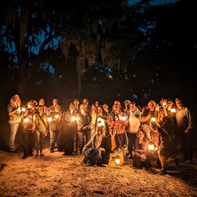 A large group of people in the dark holding lanterns on a ghost tour.