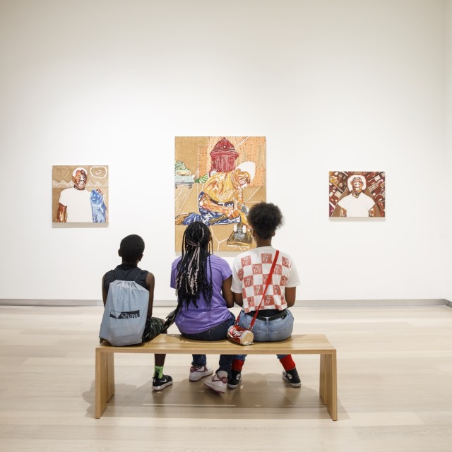 Three young children sitting on a bench admiring art work.