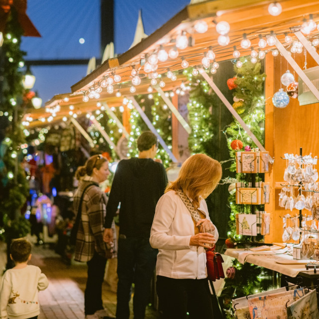 Shoppers browse festive stalls decorated with wreaths, ornaments, and twinkling lights at the Savannah Christmas Market in Plant Riverside District.