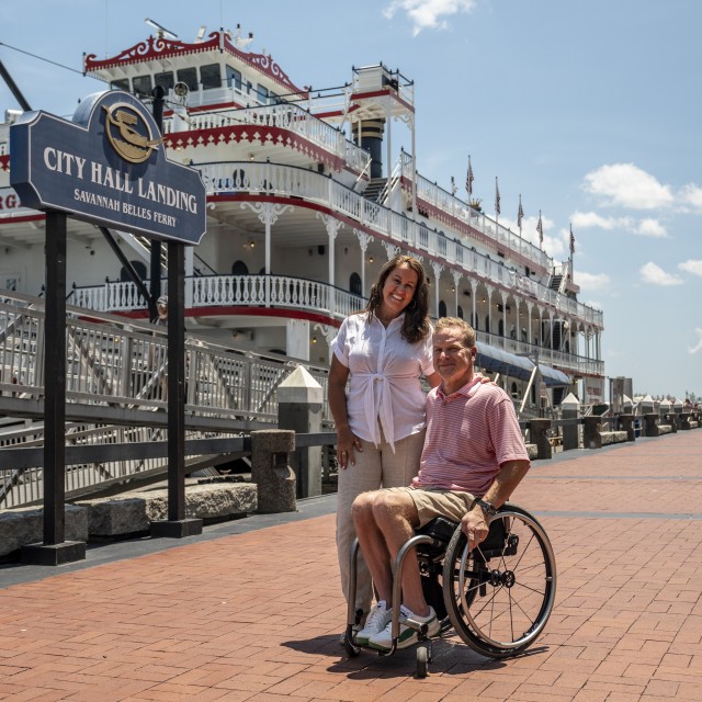 couple on river street in front of riverboat, man in wheelchair