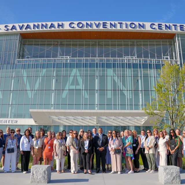 A large group posing for a photo at the front entrance of the Savannah Convention Center.