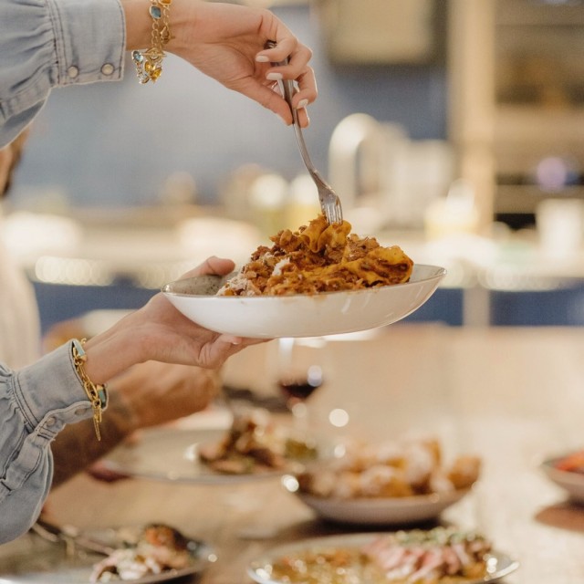 A person’s hand using a fork to twirl a large plate of pasta.