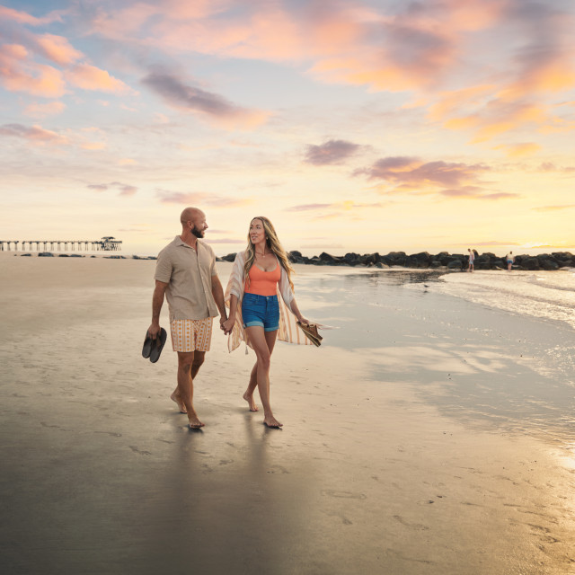 Couple holding hands while walking along Tybee Island beach at sunset.