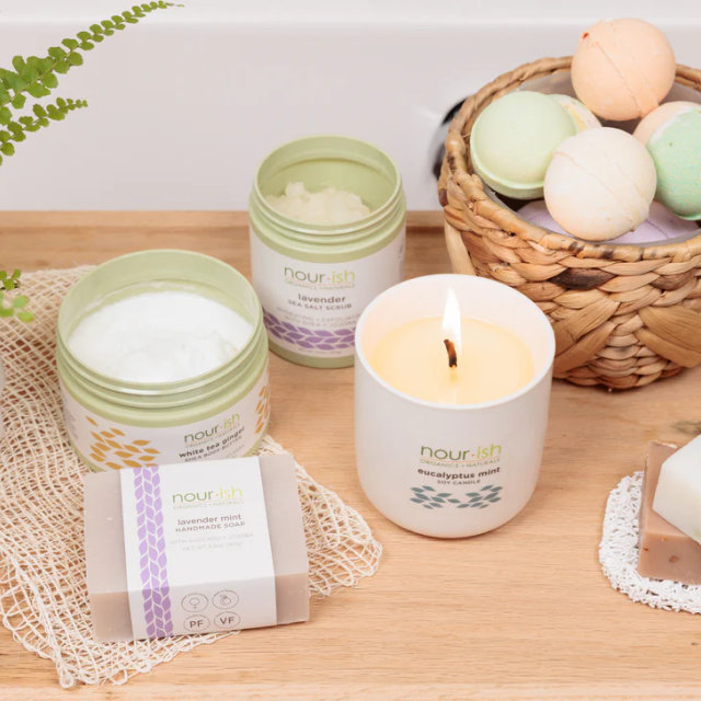 Nour-ish Savannah bath and body products including candle, soap, scrubs and bath bombs on a wooden surface.