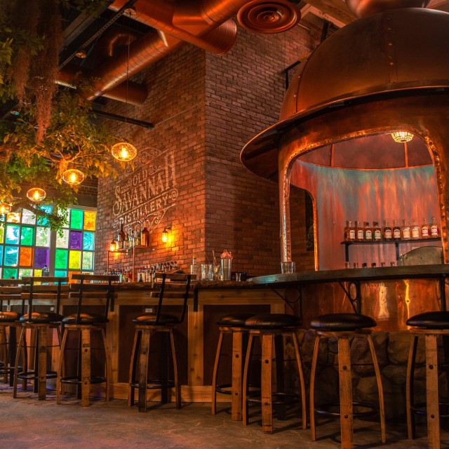 Interior of Old Savannah Distillery with copper still, bar seating, exposed brick and warm lighting.