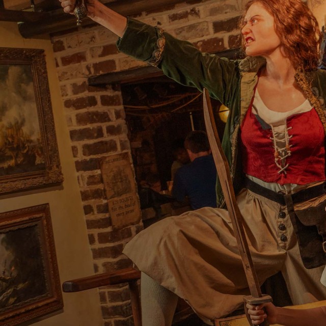 Actors in pirate costumes perform inside Savannah’s Pirates and Treasure Museum while a child smiles and holds a sword.
