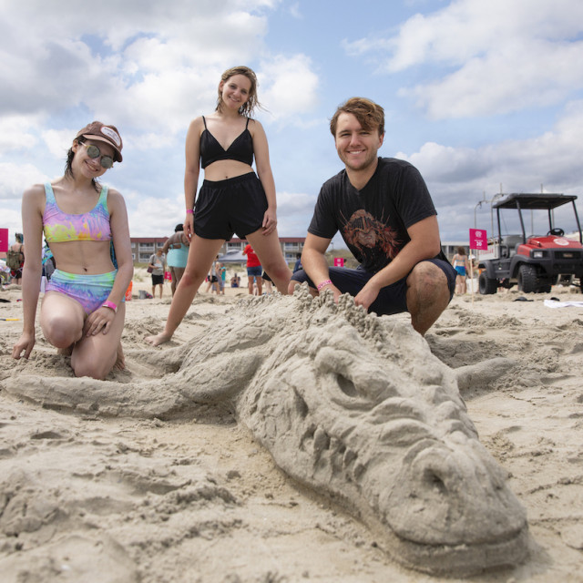 Three people pose on the beach beside a detailed sand sculpture during the SCAD Sand Arts Festival on Tybee Island.