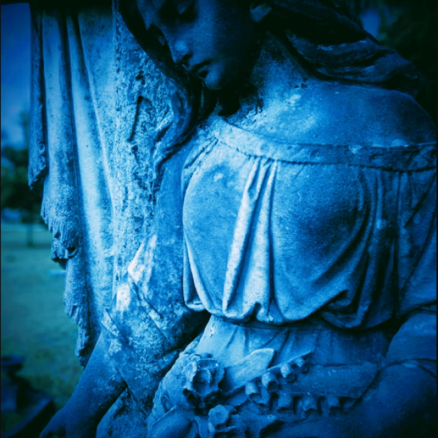 Blue-toned statue in a Savannah cemetery illuminated in eerie light.
