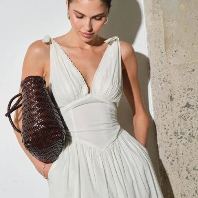 A model in a white dress and carrying a brown purse for a photo shoot