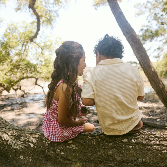 Two children sit together on a sprawling tree branch while exploring the outdoors in Savannah.
