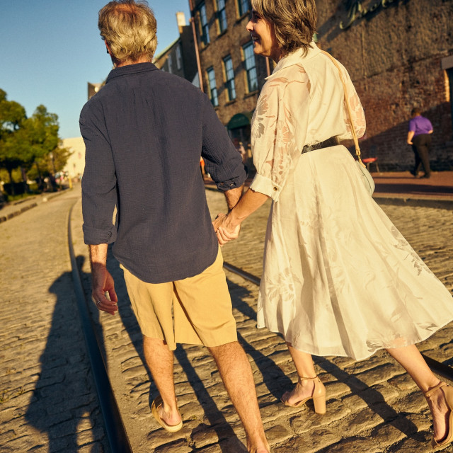 Couple holding hands while walking along the cobblestones and streetcar tracks on River Street in Savannah.