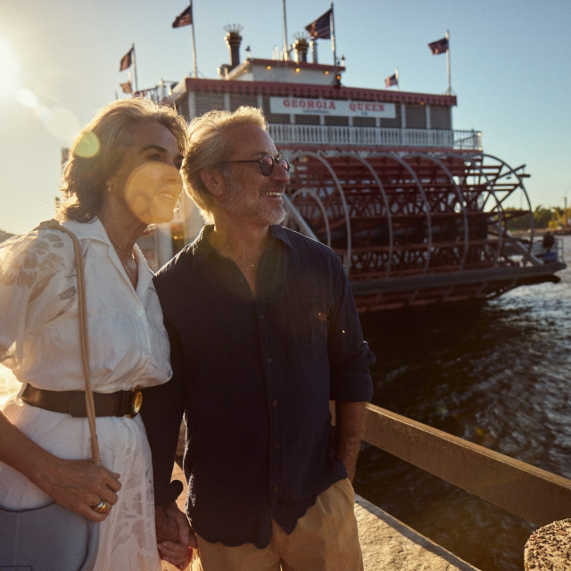 Couple standing along the Savannah riverfront with the Georgia Queen riverboat behind them.