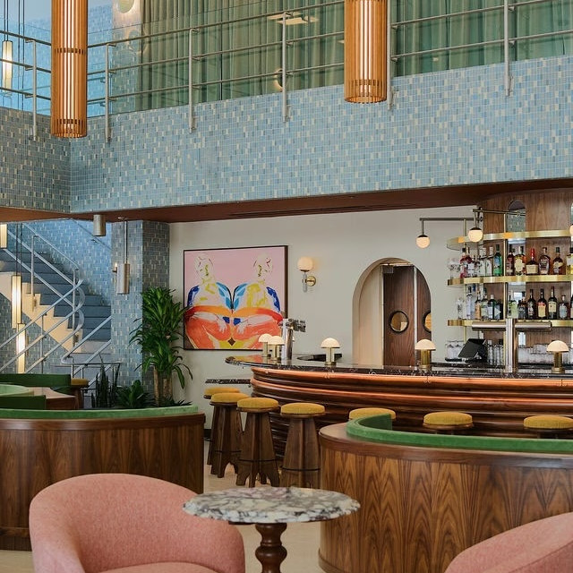 Stylish lobby bar at Municipal Grand featuring pink lounge chairs, green seating, blue tile walls and a curved wooden bar.