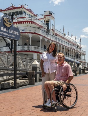 couple on river street in front of riverboat, man in wheelchair