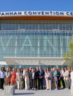 A large group posing for a photo at the front entrance of the Savannah Convention Center.