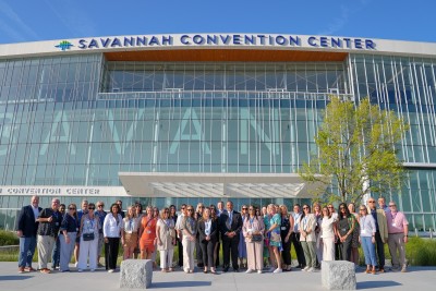 A large group posing for a photo at the front entrance of the Savannah Convention Center.