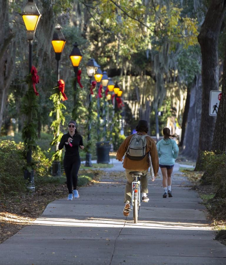 people riding bikes in Forsyth Park with holiday ribbons on lamp poless 