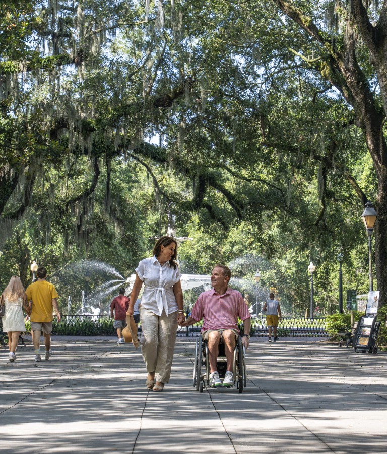 a couple walking in Forsyth Park, man in wheelchair, sunny day.