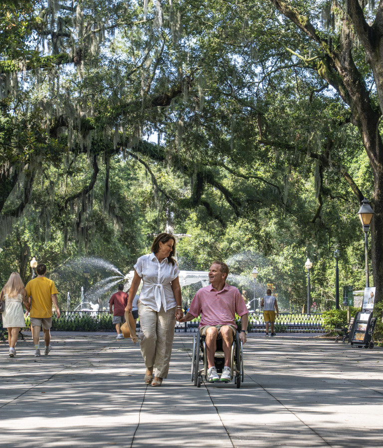 a couple walking in Forsyth Park, man in wheelchair, sunny day.