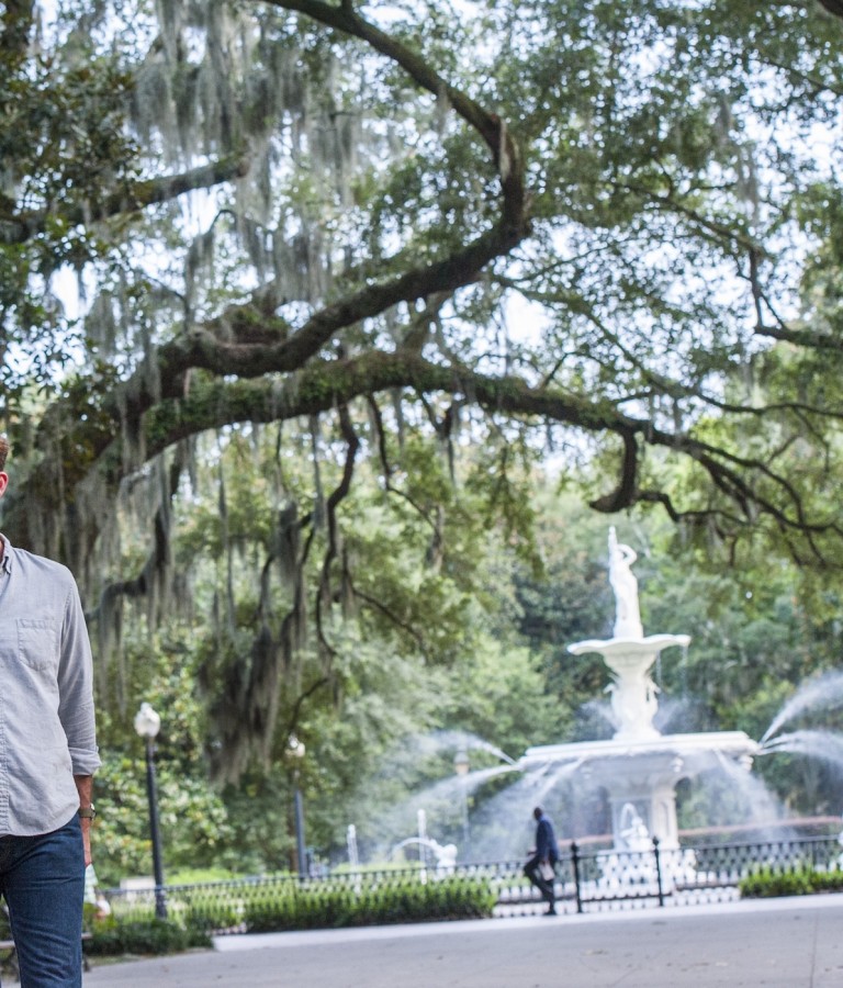 A couple walking through Forsyth Park with the fountain in the background.