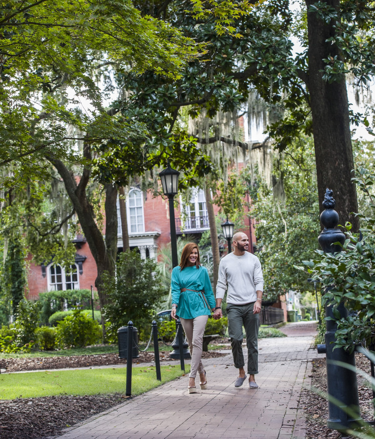 A couple walking hand in hand through Monterey Square in Savannah, GA.