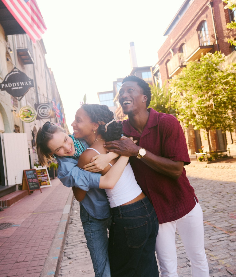 Three friends laugh and embrace together on a cobblestone street in Savannah.