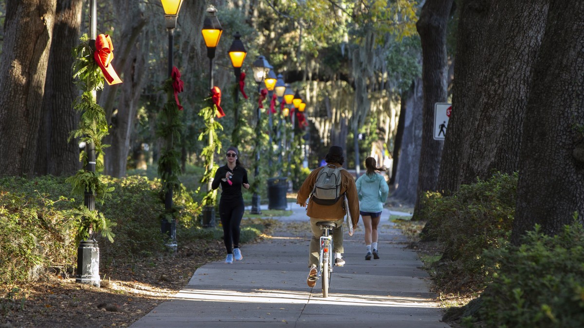 people riding bikes in Forsyth Park with holiday ribbons on lamp poless