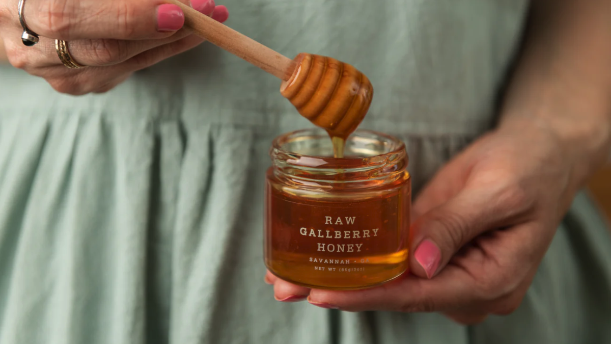 Hands holding a honey jar with honey dipper