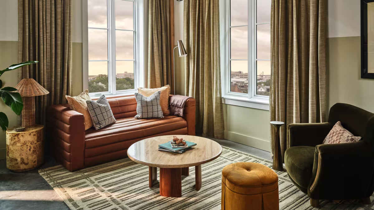 A hotel room suite living room with seating, coffee table and large windows.