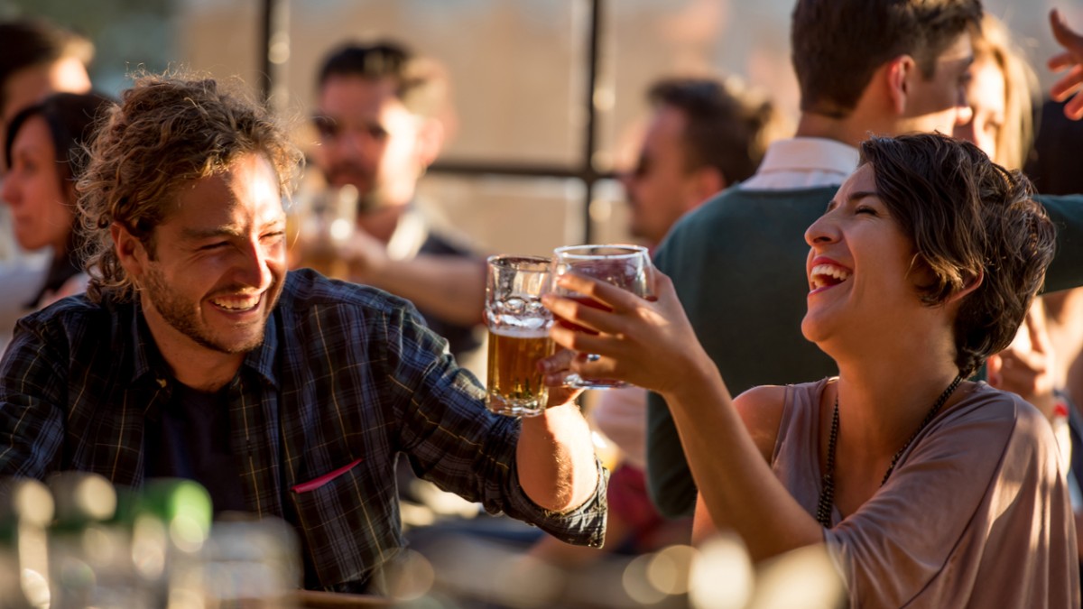 A man and a woman cheering with drinks in a lively restaurant.