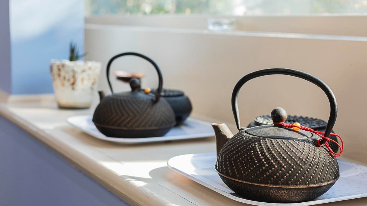 A row of tea kettles sitting along a window sill.