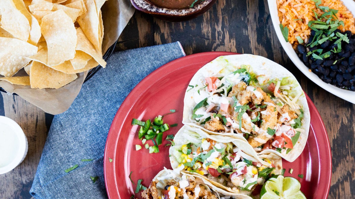 A plate of three soft tacos, chips and salsa, beans and rice on a table.