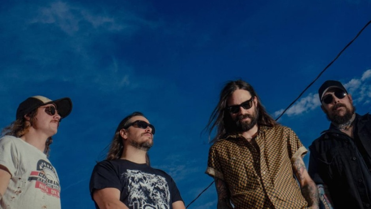 A four man band posing together with a dark sky in the background.