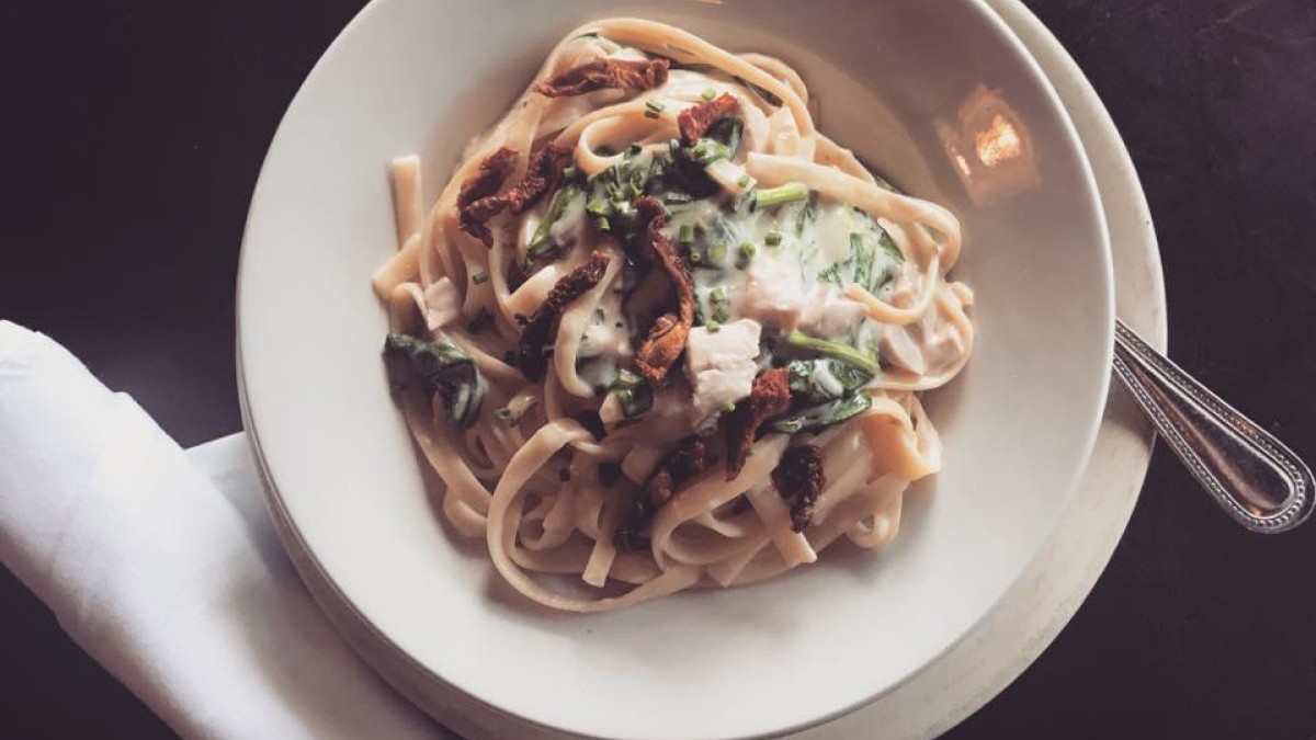 A plate of alfredo pasta with mushrooms and spinach.
