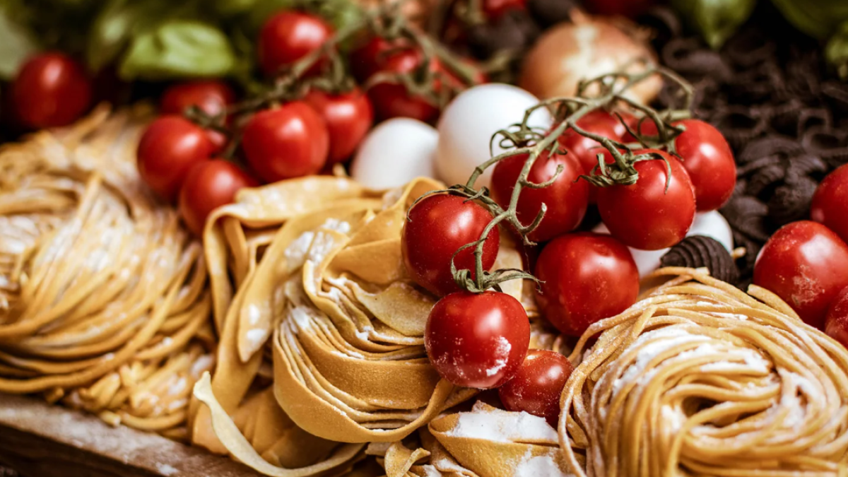 Numerous types of uncooked pasta and fresh cherry tomatoes.