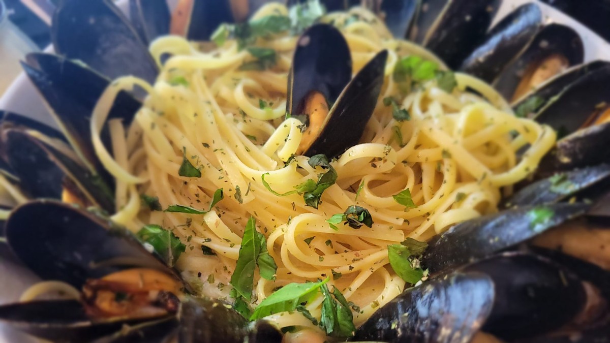 A plate of steamed mussels with pasta in a white wine sauce.