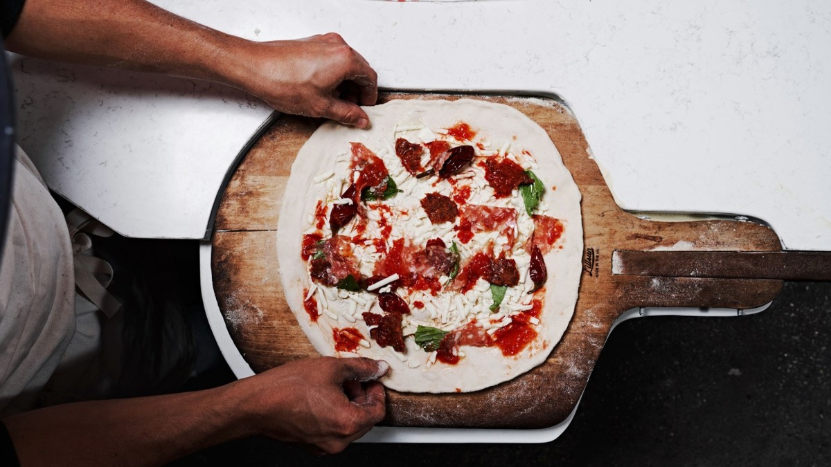 A pizza on a wooden peel prepped for a wood-fired oven.